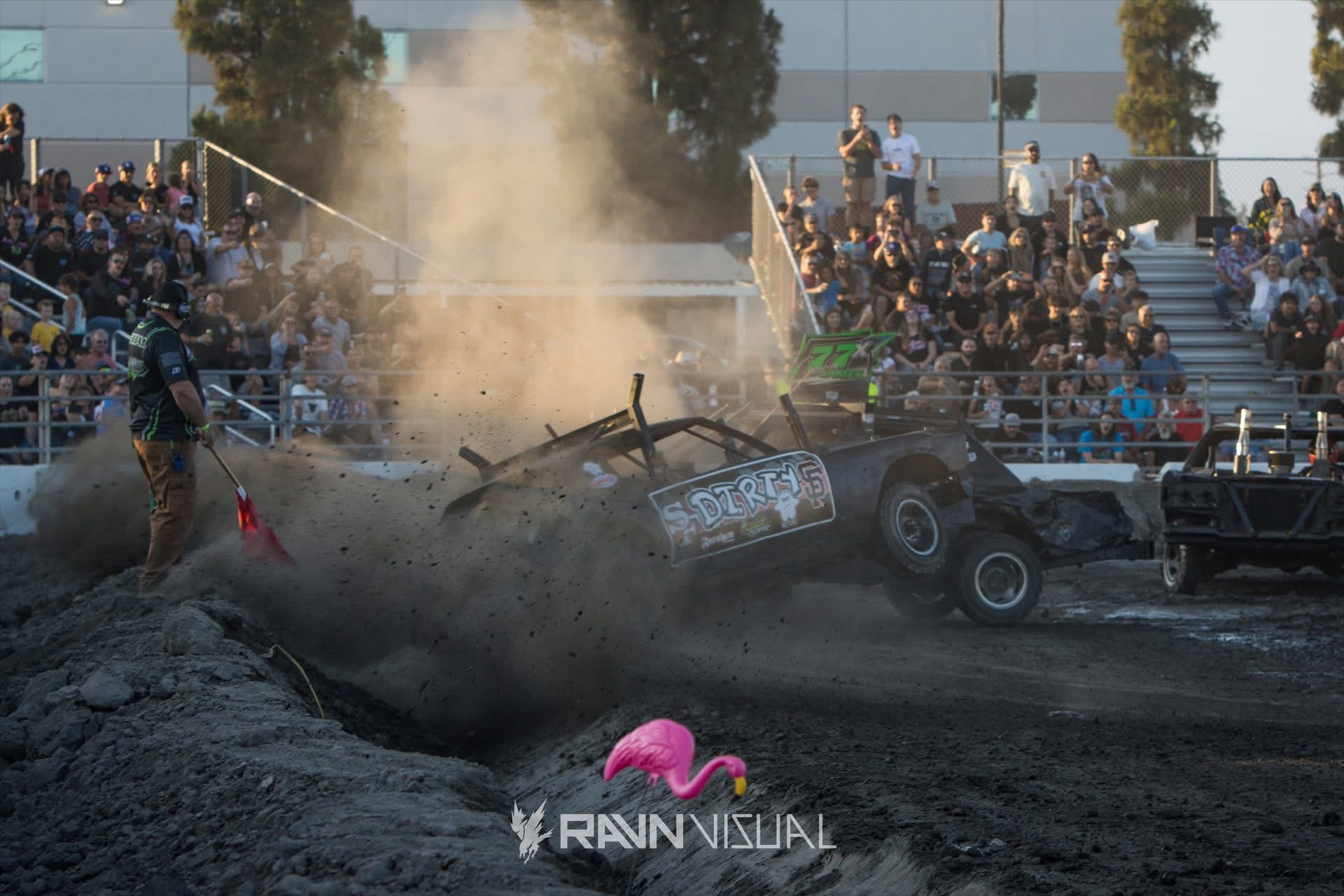 Demolition derby cars competing in a dirt arena in front of spectators